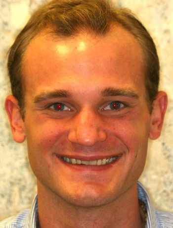 Smiling young man with short light brown hair against a neutral background.