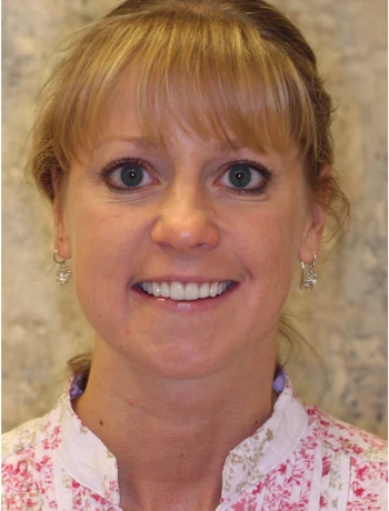 Smiling woman with light brown hair, bangs, wearing star-shaped earrings and a white top with pink floral pattern.