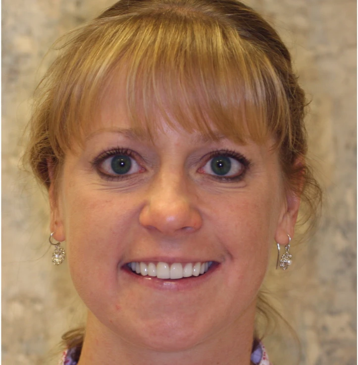 Close-up of a smiling woman with blonde hair, green eyes, and wearing dangling earrings.