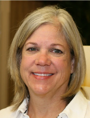 Smiling middle-aged woman with shoulder-length gray hair wearing a white shirt.