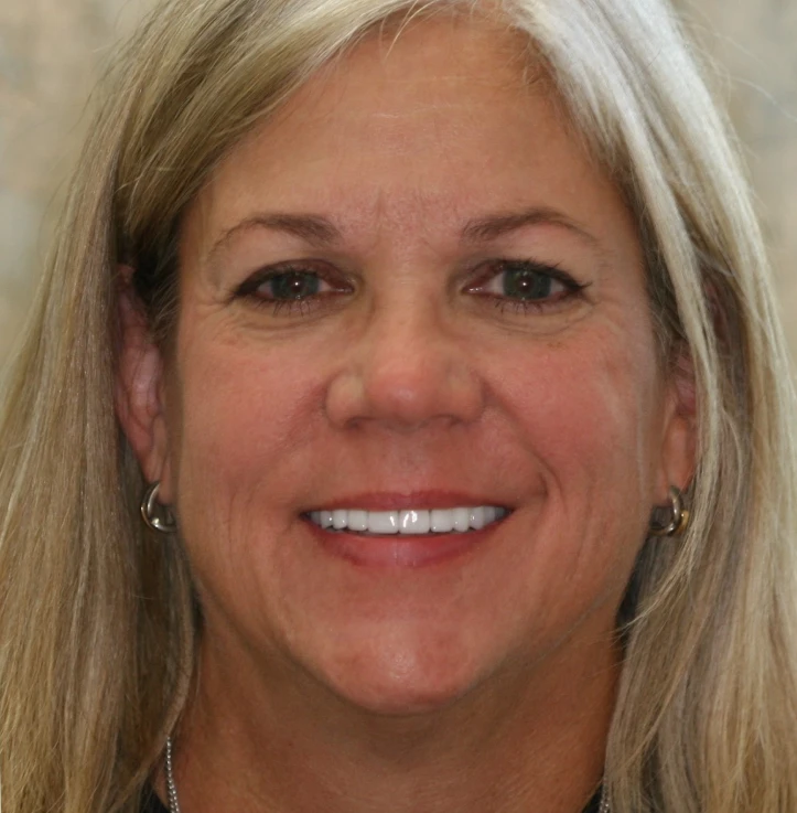Smiling middle-aged woman with straight blonde hair and hoop earrings, looking directly at the camera.