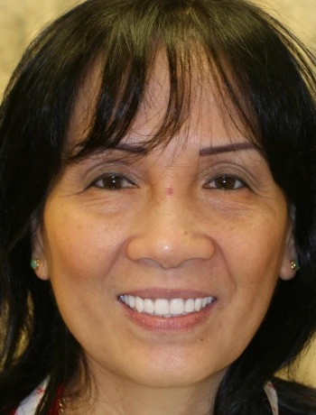 Close-up portrait of a smiling middle-aged Asian woman with dark hair and green earrings.