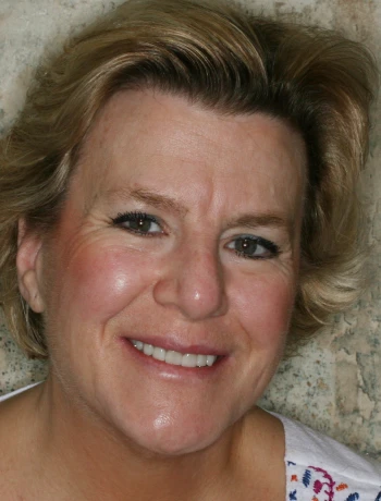 Close-up of a smiling middle-aged woman with short blonde hair against a stone background.