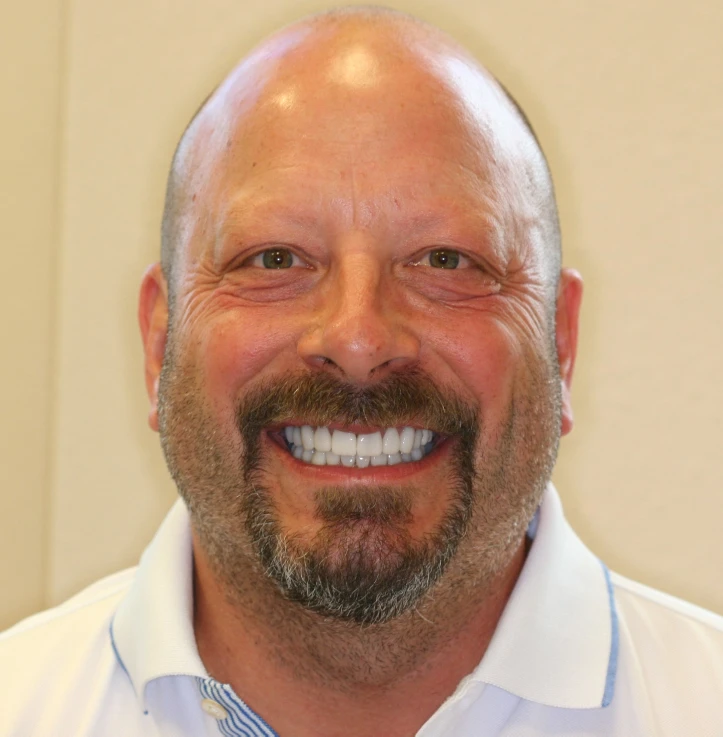 Smiling bald man with a dark beard wearing a white collared shirt.
