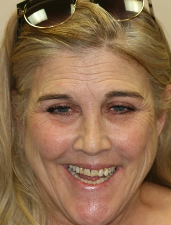 Smiling middle-aged woman with blonde hair and sunglasses resting on her head.