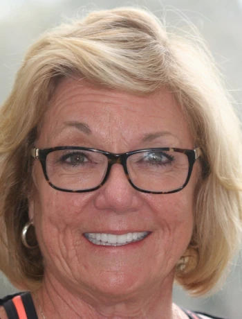 Smiling older woman with short blonde hair and black glasses.