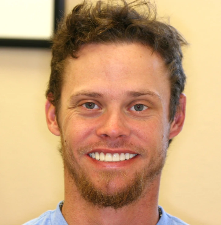 Close-up of a smiling man with short curly hair and a goatee wearing a light blue shirt.