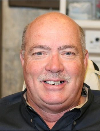 Smiling middle-aged bald man with a mustache wearing a dark collared shirt.