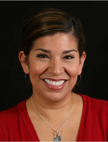 Smiling woman with dark hair pulled back, wearing a red top and silver necklace against a black background.