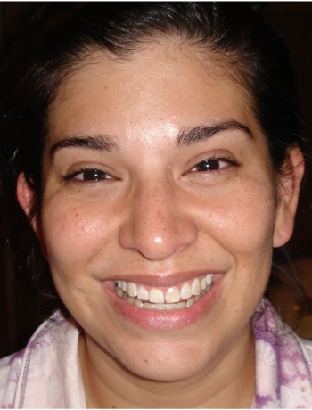 Close-up of a smiling woman with dark hair and brown eyes, wearing a light-colored top.