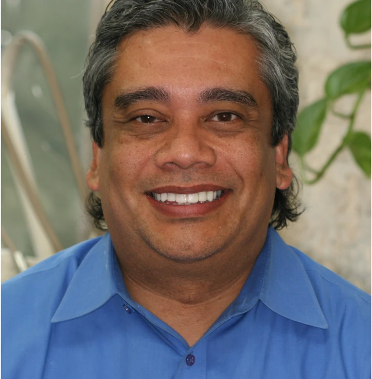 Smiling middle-aged man with salt-and-pepper hair wearing a blue collared shirt.