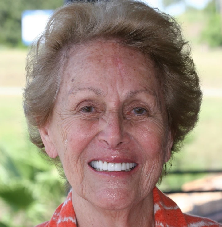 Close-up of a smiling elderly woman with short curly hair, wearing an orange patterned scarf.