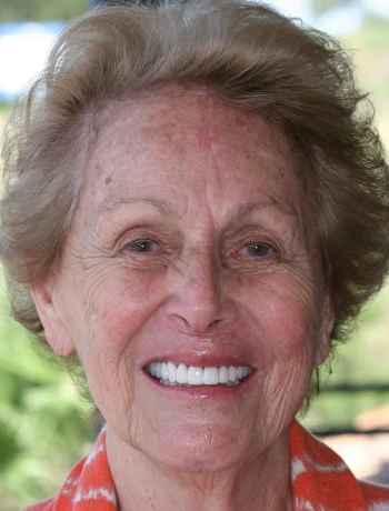 Smiling elderly woman with short hair and wearing an orange patterned scarf.