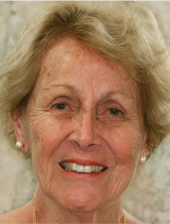 Smiling elderly woman with short gray hair and pearl earrings.