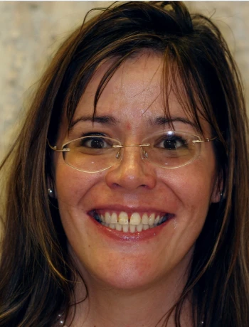 Smiling woman with long brown hair and glasses, showing teeth.