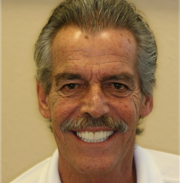 Smiling older man with gray hair and mustache wearing a white shirt.