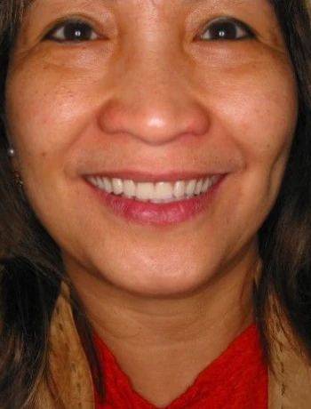 Close-up portrait of a smiling woman with dark hair wearing a red top and tan jacket.