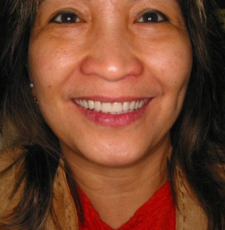 Close-up of a smiling woman with dark hair, wearing a red scarf and tan jacket.