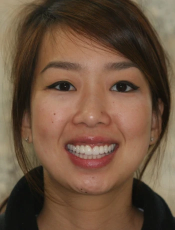 Smiling woman with dark hair, winged eyeliner, and visible teeth against a blurred light background.