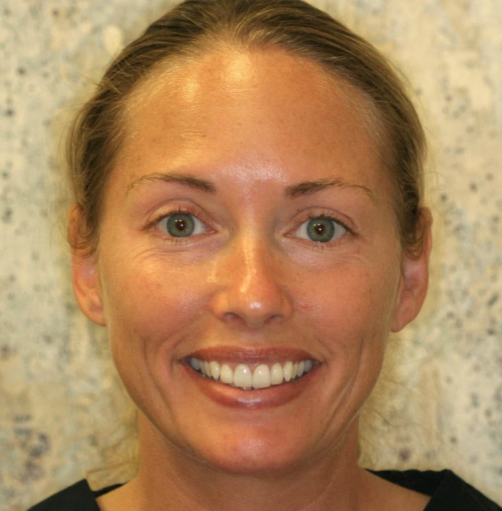 Smiling woman with light skin, green eyes, and pulled-back light brown hair against a textured beige background.