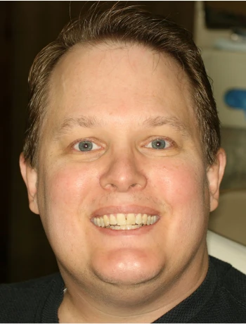 Close-up of a smiling man with light skin, blue eyes, and short brown hair.