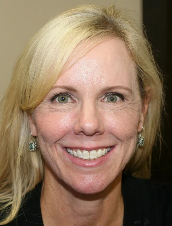Smiling middle-aged woman with blonde hair, green eyes, and green stone earrings.