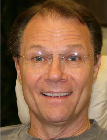 Smiling middle-aged man with glasses sitting indoors.