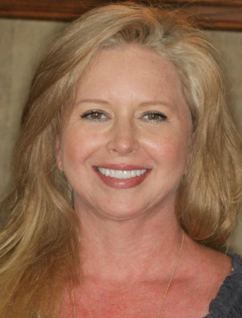 Smiling woman with long blonde hair and light makeup wearing a blue top.