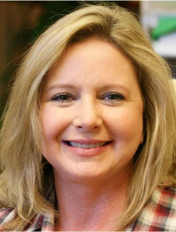 Smiling middle-aged woman with blonde hair wearing a plaid shirt.
