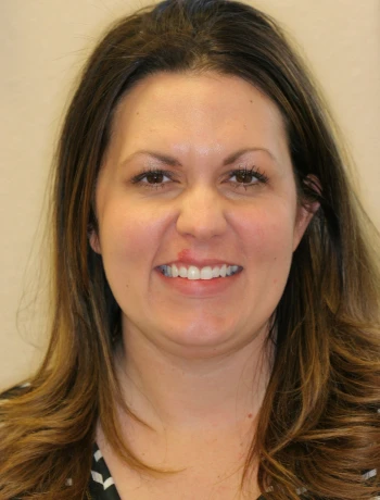 Woman with long brown hair smiling against a plain beige background.