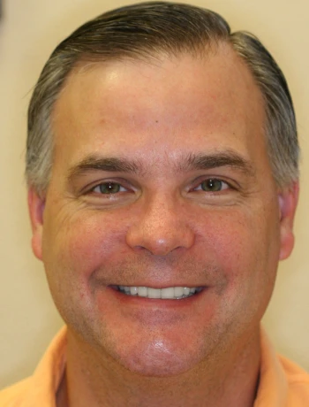 Smiling middle-aged man with short dark hair and wearing an orange shirt.