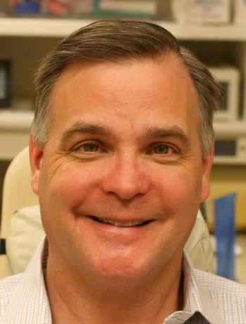 Smiling middle-aged man with short brown hair wearing a light-colored collared shirt.