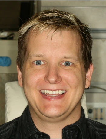 Smiling man with short blond hair and blue eyes wearing a black collared shirt.