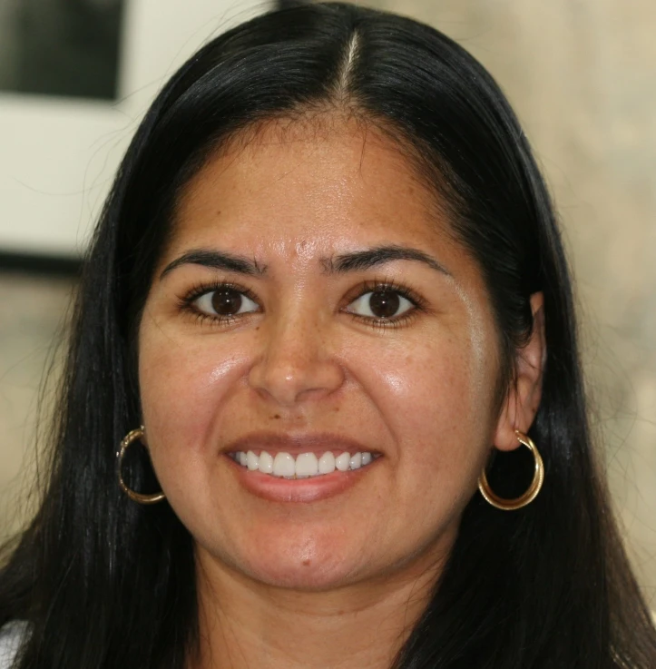 Smiling woman with long black hair, brown eyes, and gold hoop earrings, in a close-up portrait.
