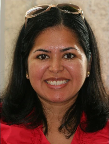 Smiling woman with long black hair, wearing a red top and sunglasses on her head.