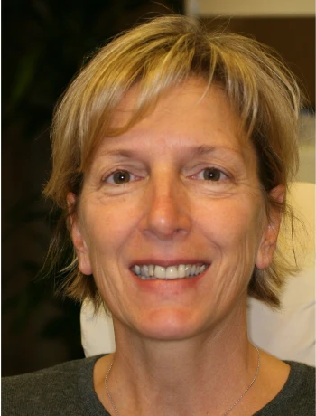 Smiling middle-aged woman with short blonde hair wearing a grey top.