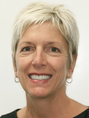 Smiling middle-aged woman with short blonde hair wearing hoop earrings and a black top.