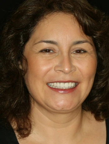 Smiling woman with curly dark hair and brown eyes against a black background.