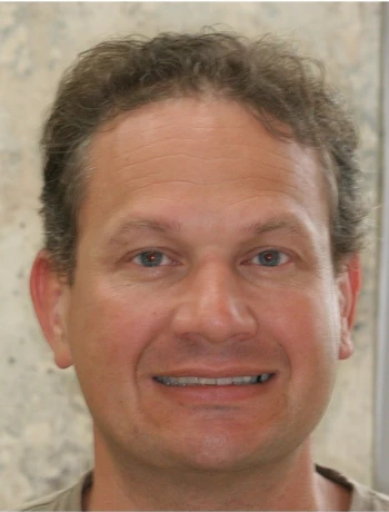 Close-up of a middle-aged man with curly brown hair smiling slightly in front of a neutral background.