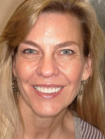 Close-up portrait of a smiling blonde woman with blue eyes and wearing hoop earrings.
