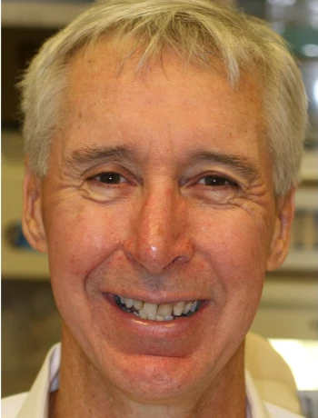 Smiling middle-aged man with short gray hair and wrinkles around his eyes.