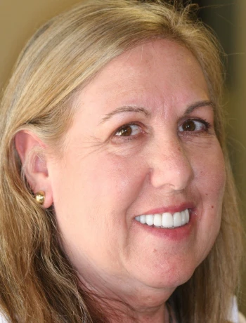 Close-up portrait of a smiling middle-aged woman with long blonde hair and gold stud earrings.