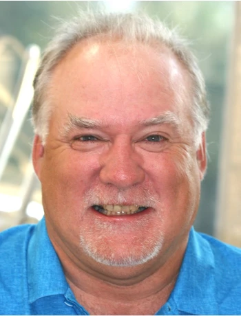 Smiling middle-aged man with gray hair and goatee wearing a blue shirt.
