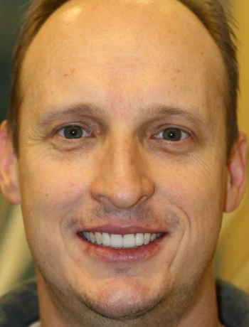 Close-up of a smiling man with light skin, short brown hair, and green eyes.