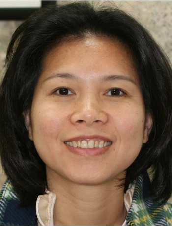 Smiling woman with dark hair wearing a plaid scarf and light jacket against a neutral background.