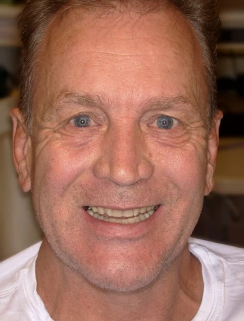 Smiling middle-aged man with short brown hair and blue eyes wearing a white shirt.