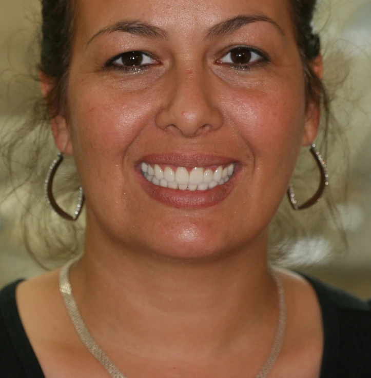 Close-up of a smiling woman with hoop earrings and a silver necklace.