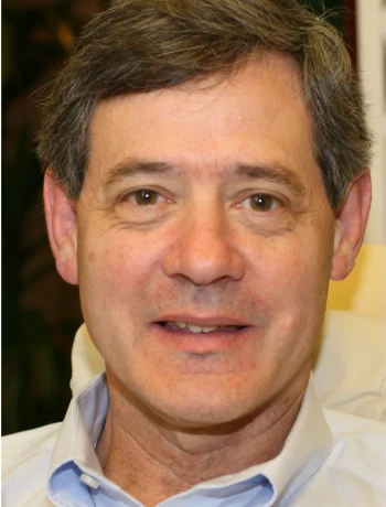Middle-aged man with short brown hair smiling, wearing a light blue collared shirt.