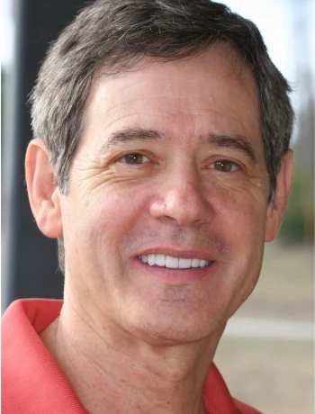 Middle-aged man with short gray hair wearing a red collared shirt, smiling outdoors.