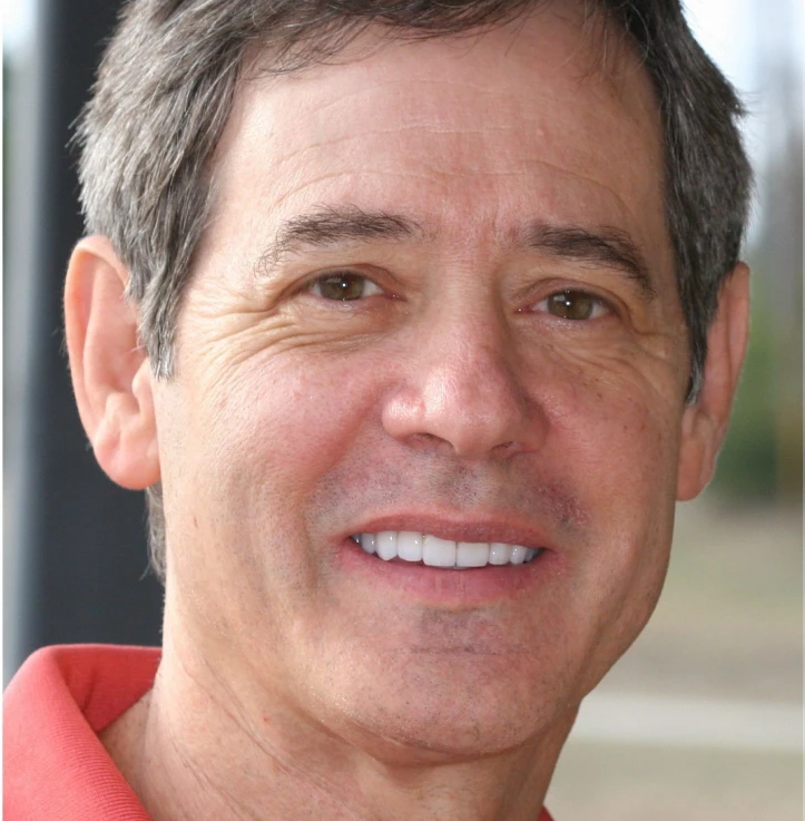 Close-up of a middle-aged man with short graying hair smiling and wearing a red collared shirt.